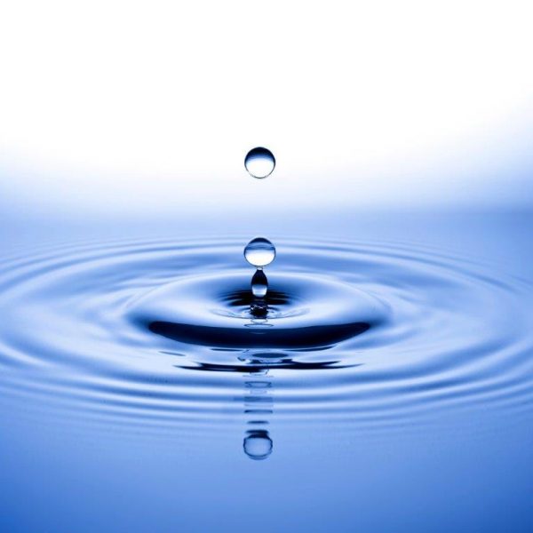 Wassertropfen fällt in ruhiges Wasser und erzeugt kleine Wellen